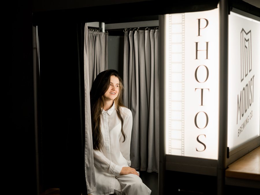 A guest sitting inside our enclosed photo booth with the lit PHOTOS light box